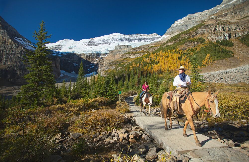 People on a guided horseback riding tour in Lake Louise with Victoria Glacier in the background